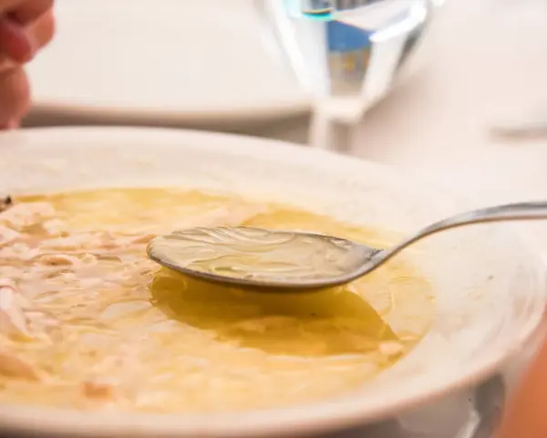 Caldo de pollo casero en un plato blanco con una cuchara.