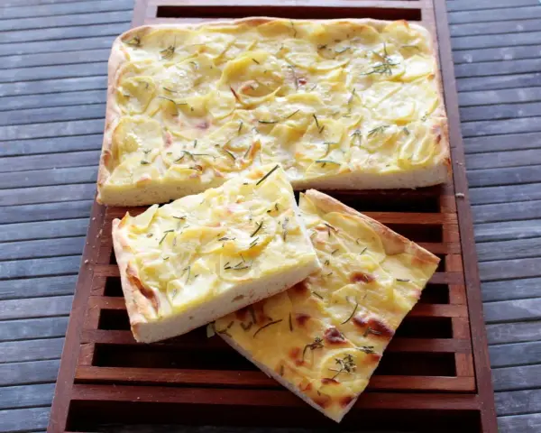 Focaccia con lievito istantaneo, ricca di patate e rosmarino, servita su un tagliere di legno.