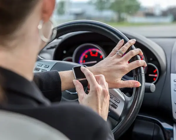 Frau tippt auf ihre Smartwatch am Steuer. Handy am Steuer Strafe vermeiden!