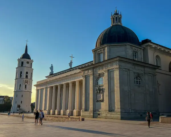 Wileńskie kościoły: Katedra i dzwonnica na placu. Słońce oświetla monumentalną architekturę, tworząc długie cienie.