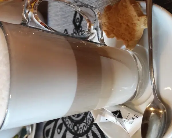 Kawa latte w szklance, obok ciasteczko i cukier. Idealna na przerwę w karczmie u wróbla menu.