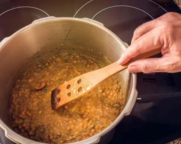 Lentejas deliciosas cocinándose en olla express, removidas con cuchara de madera.