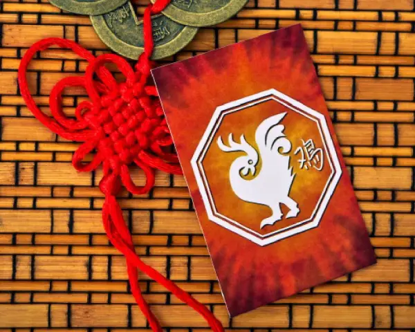 Czerwony sznur szczęścia i karta z białym kogutem, symbolem chińskiego zodiaku, na tle bambusowej maty.
