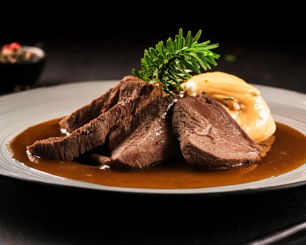 Zartes Tafelspitz-Rezept auf einem Teller mit Sauce, Beilage und Rosmarinzweig.