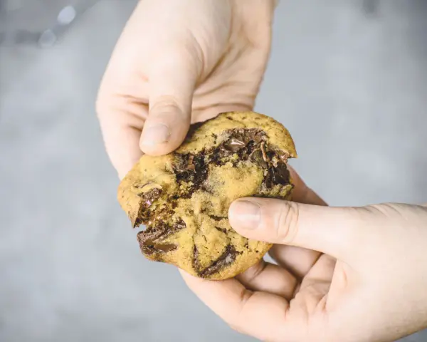 Hände halten einen frisch gebackenen American Cookie mit geschmolzener Schokolade. Perfekt zum amerikanischen Cookies backen!