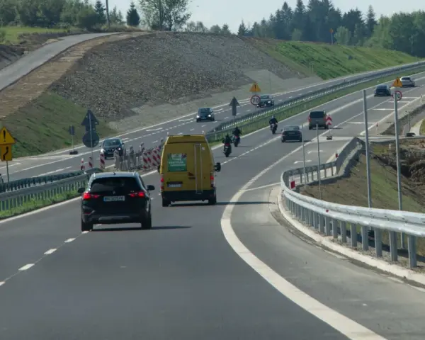 Droga ekspresowa z samochodami i motocyklami, gdzie panuje bezpieczna prędkość. W tle widać prace budowlane.