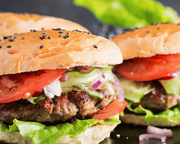 Dwa soczyste burgery wołowe z bułką, pomidorem, sałatą i ogórkiem.