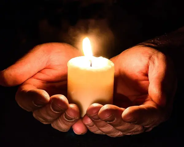 Hände halten eine brennende Kerze, ein Symbol für den Totensonntag, das Licht und Erinnerung spendet.