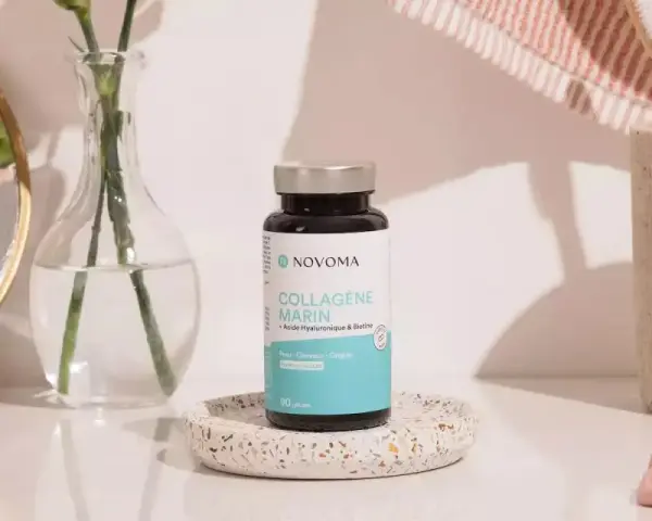 Flacon de cure de collagène marin Novoma, posé sur un plateau décoratif, près d'un miroir, d'une fleur et d'une brosse à dents.
