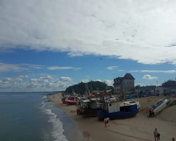 Chłopy trasa: łodzie rybackie na plaży, budynek z czerwonym dachem, morze i niebo z chmurami.