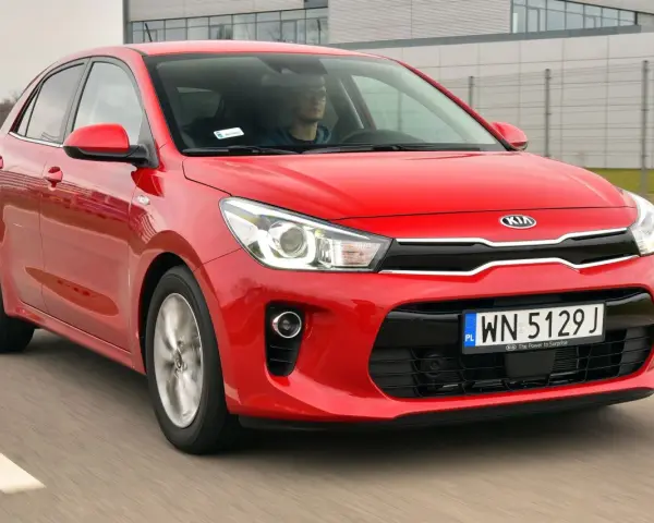 Czerwony Kia Rio w ruchu. Kierowca w okularach za kierownicą. Wiele pozytywnych kia rio opinie o tym modelu.