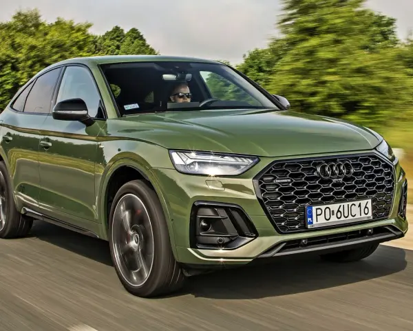 Zielone Audi Q5 Sportback z silnikiem 50 TFSI jedzie po drodze. Kierowca w okularach przeciwsłonecznych prowadzi auto.