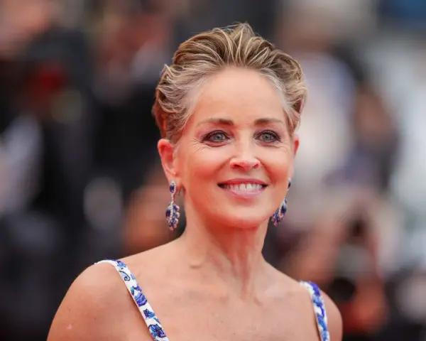 Sharon Stone luce un elegante corte bixie, con pendientes de zafiro y un vestido blanco con detalles azules.