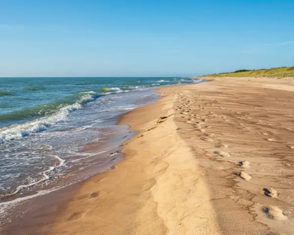 Spokojne, dzikie plaże nad Bałtykiem. Fale delikatnie obmywają piaszczysty brzeg, a na piasku widoczne są ślady stóp.
