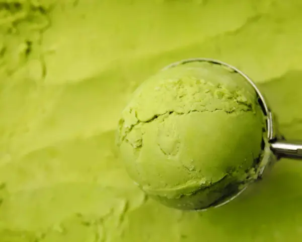 Eine Kugel cremiges Matcha-Eis wird mit einem Löffel aus einer Schüssel gehoben. Perfekt für ein erfrischendes Matcha Eis Rezept.