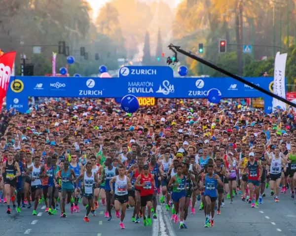 Multitudinaria salida del maratón Sevilla 2026, con miles de corredores bajo el arco de meta.
