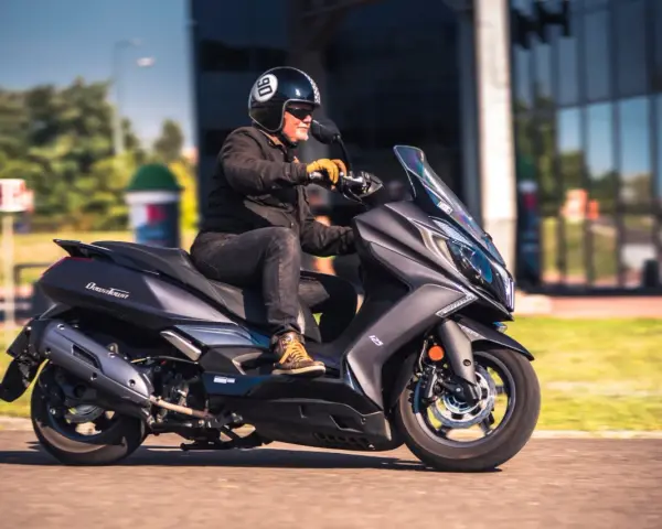 Mężczyzna w kasku jedzie na skuterze Kymco Downtown 125. Poznaj kymco downtown 125 dane techniczne.