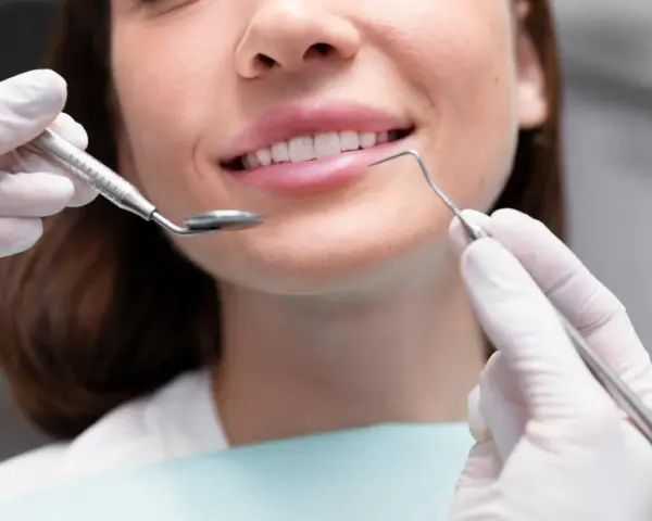Uśmiechnięta kobieta podczas zabiegu remineralizacji szkliwa. Dentysta używa lusterka i sondy.