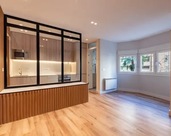 Entrada salón recibidor integrado. Cocina moderna con cristalera y madera, conectada a un luminoso salón con ventanas.
