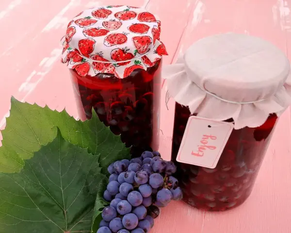 Słoiki z przetworami z winogron, przypominającymi wino z mrożonych winogron. Obok kiść winogron i liście.