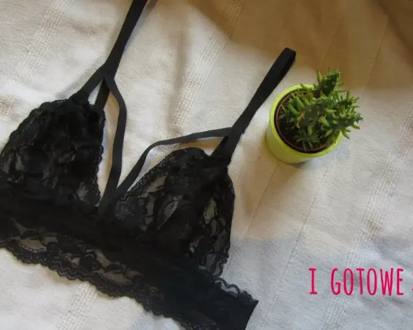Czarny, koronkowy biustonosz typu bralette, idealny do obszywania bielizny. Obok mała roślinka w doniczce.