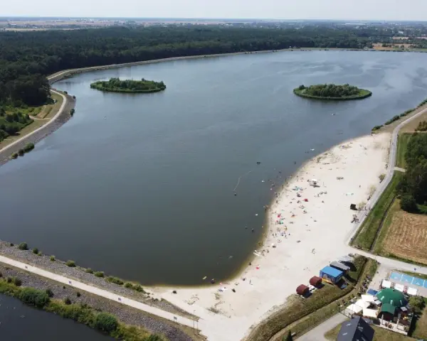 Opolskie atrakcje: piaszczysta plaża nad jeziorem, wyspy, las i mostek. Ludzie odpoczywają i kąpią się.