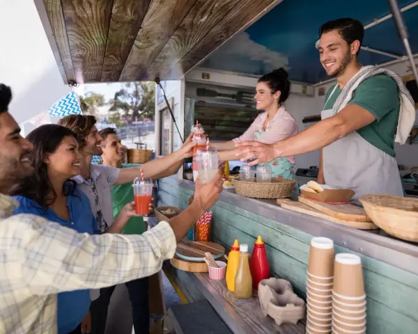 Uśmiechnięci ludzie odbierają napoje od barmanów z food trucka.
