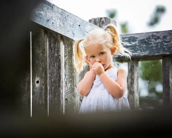 Mała dziewczynka z blond kucykami ssie kciuk, co może być sygnałem, że rodzice zastanawiają się, jak oduczyć dziecko ssania kciuka.