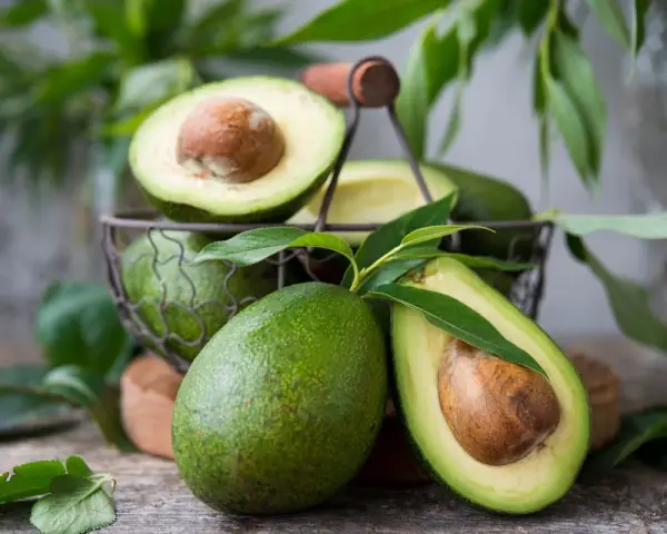 Des avocats frais, entiers et coupés en deux, dans un panier. Pour savoir comment avoir un avocatier qui donne des fruits, il faut de la patience et de bons soins.