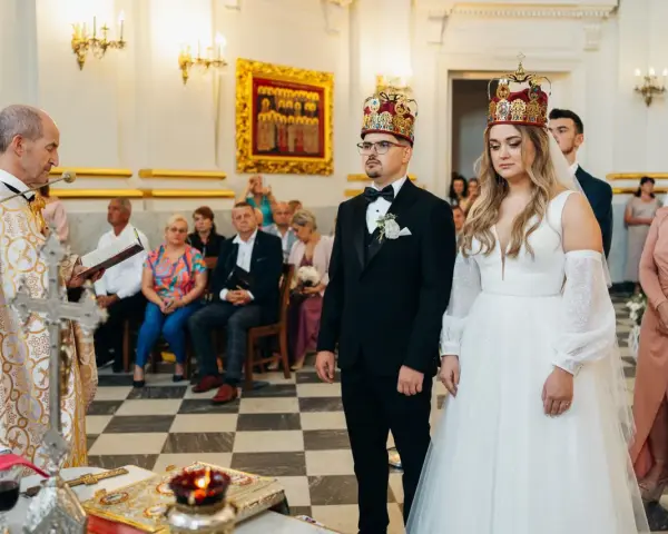 Uroczystość zaślubin w cerkwi. Pan młody, niczym ludowy grajek z Ukrainy, w eleganckim czarnym garniturze, z narzeczoną w białej sukni, przyjmują błogosławieństwo.