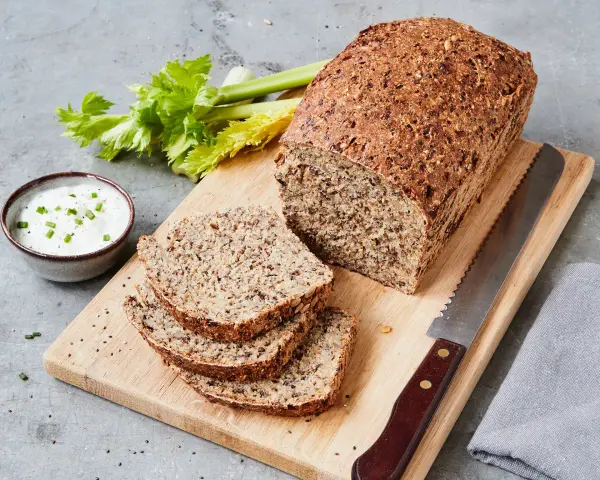 Ein rustikales Chia Brot, frisch aufgeschnitten, mit Sellerie und Dip auf einem Holzbrett.