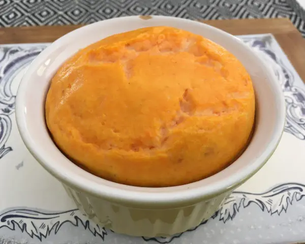 Un délicieux flan de carottes, doré et moelleux, servi dans un ramequin blanc sur une assiette décorée.