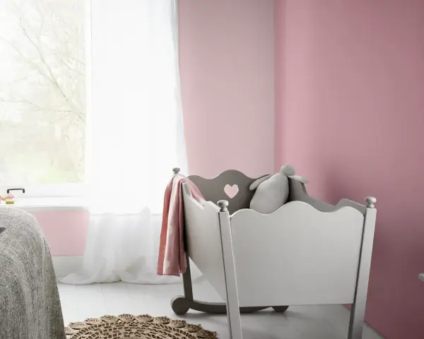 Pokój dziecięcy z łóżeczkiem, pluszowym królikiem i kocem w kolorze amarant. Ściany pomalowane na delikatny róż.