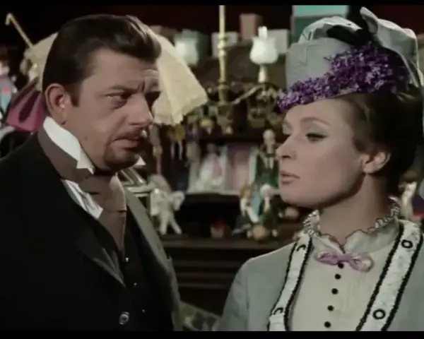 Mariusz Dmochowski w filmach, u boku pięknej kobiety w kapeluszu, w sklepie pełnym lalek i bibelotów.