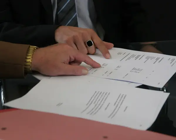 Dwóch mężczyzn analizuje dokumenty. Jeden z nich, w garniturze i z pierścieniem na palcu, wskazuje na tabelę. Pytanie: Millennium Bank zajęcie egzekucyjne jak sprawdzić?