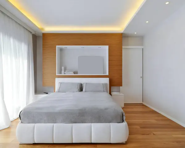 Camera da letto con letto bianco, lenzuola grigie e un moderno controsoffitto con illuminazione a LED.
