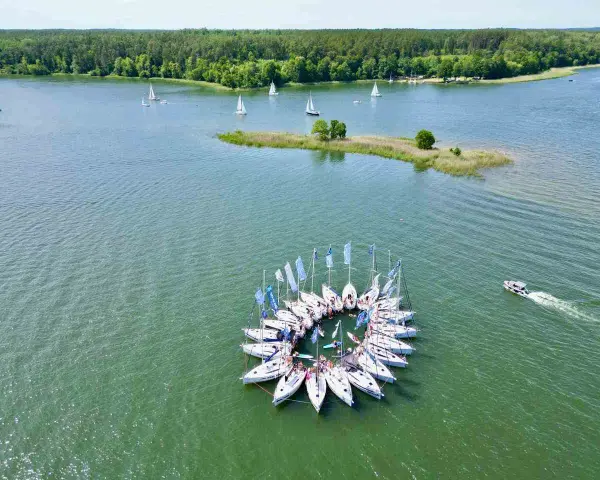 Żaglówki tworzą okrąg na jeziorze, otoczone lasem. To jedne z najpiękniejszych miejsc w Polsce – Mazury.