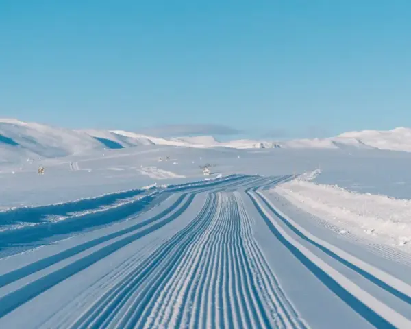 Perfekt preparerade spår för längdskidåkning i Hemsedal. Solen lyser på de snötäckta bergen och den blå himlen.
