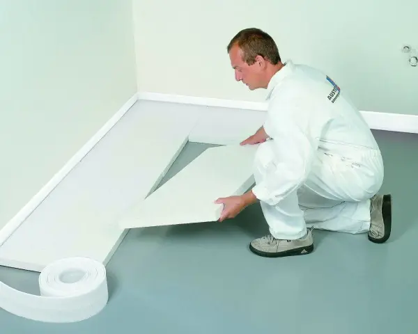 Mężczyzna w białym kombinezonie układa styropian na podłodze.