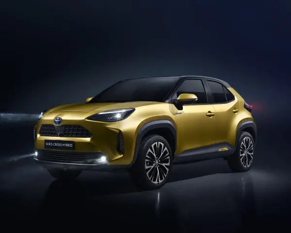 Złoty Toyota Yaris Cross Hybrid z włączonymi światłami na ciemnym tle.