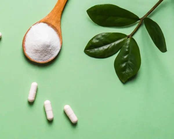 Vita C-vitaminer i kapslar och pulver på en sked, med gröna blad.