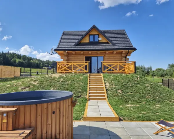 Uroczy domek na odludziu z drewnianą werandą i schodami prowadzącymi do drzwi. Przed domkiem jacuzzi i leżaki.