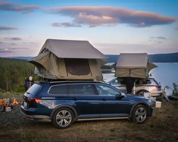 Två bilar med takboxar som fungerar som tält står redo för camping vid en sjö. En eld sprakar i förgrunden. En perfekt plats för camping i Gnesta.