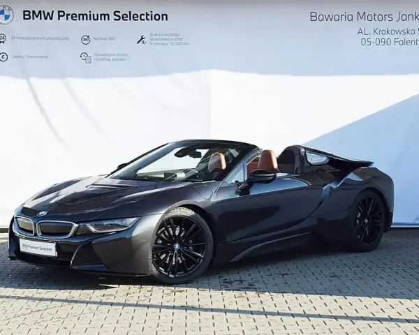 Ciemnoszary kabriolet BMW i8 z brązowym wnętrzem na tle białej ściany z logo BMW.