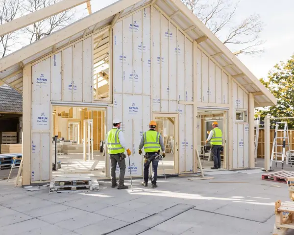 Construction d'une maison écologique passive en bois. Des ouvriers en gilets de sécurité supervisent le chantier.