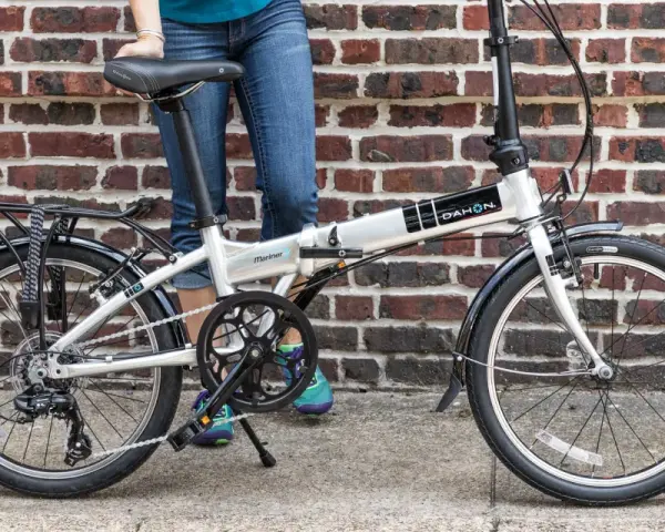 A person stands next to a silver Dahon Mariner folding commuting bike, ready for their next urban adventure.