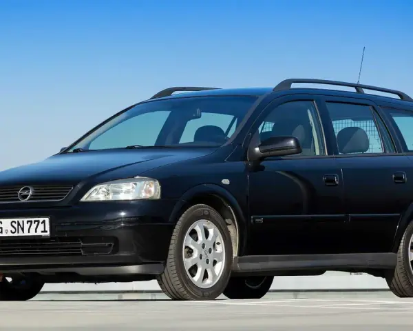 Schwarzer Opel Astra Kombi, alt, mit Dachreling und Kennzeichen GG SN 771, parkt auf einem Parkdeck vor blauem Himmel.