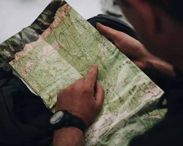 Un randonneur consulte une carte IGN des plateaux du Vercors, pointant un chemin sur le terrain.