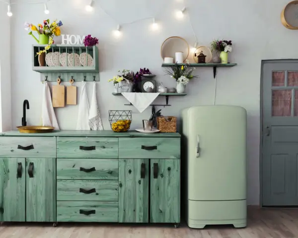 Cocina rústica con muebles de madera pintados en pintura a la tiza verde, un refrigerador vintage y una puerta gris.