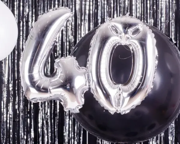 Srebrne balony z cyfrą 40 i biały balon na tle błyszczącej kurtyny. Idealne na zabawy na 40 urodziny!